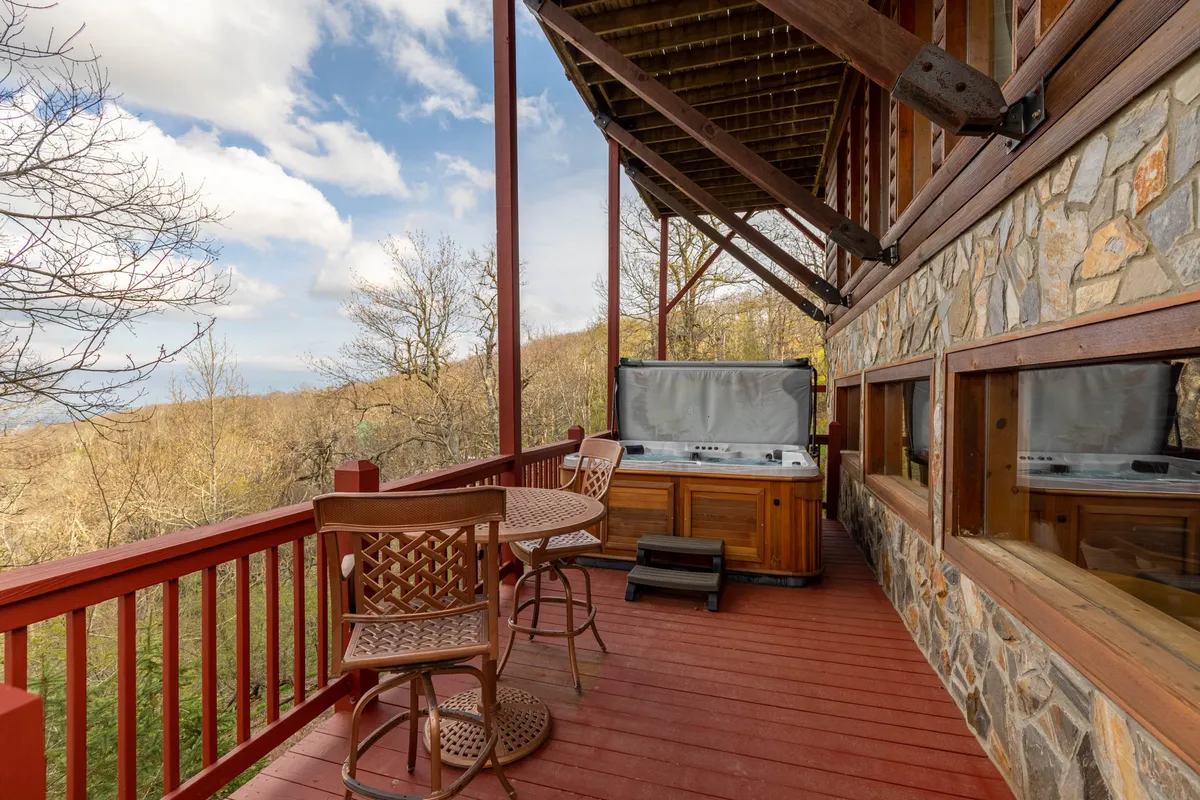 This exterior image captures a wooden deck featuring a saltwater hot tub and outdoor seating, with breathtaking mountain views in the background. The scene suggests relaxation and socializing while being immersed in the natural landscape.