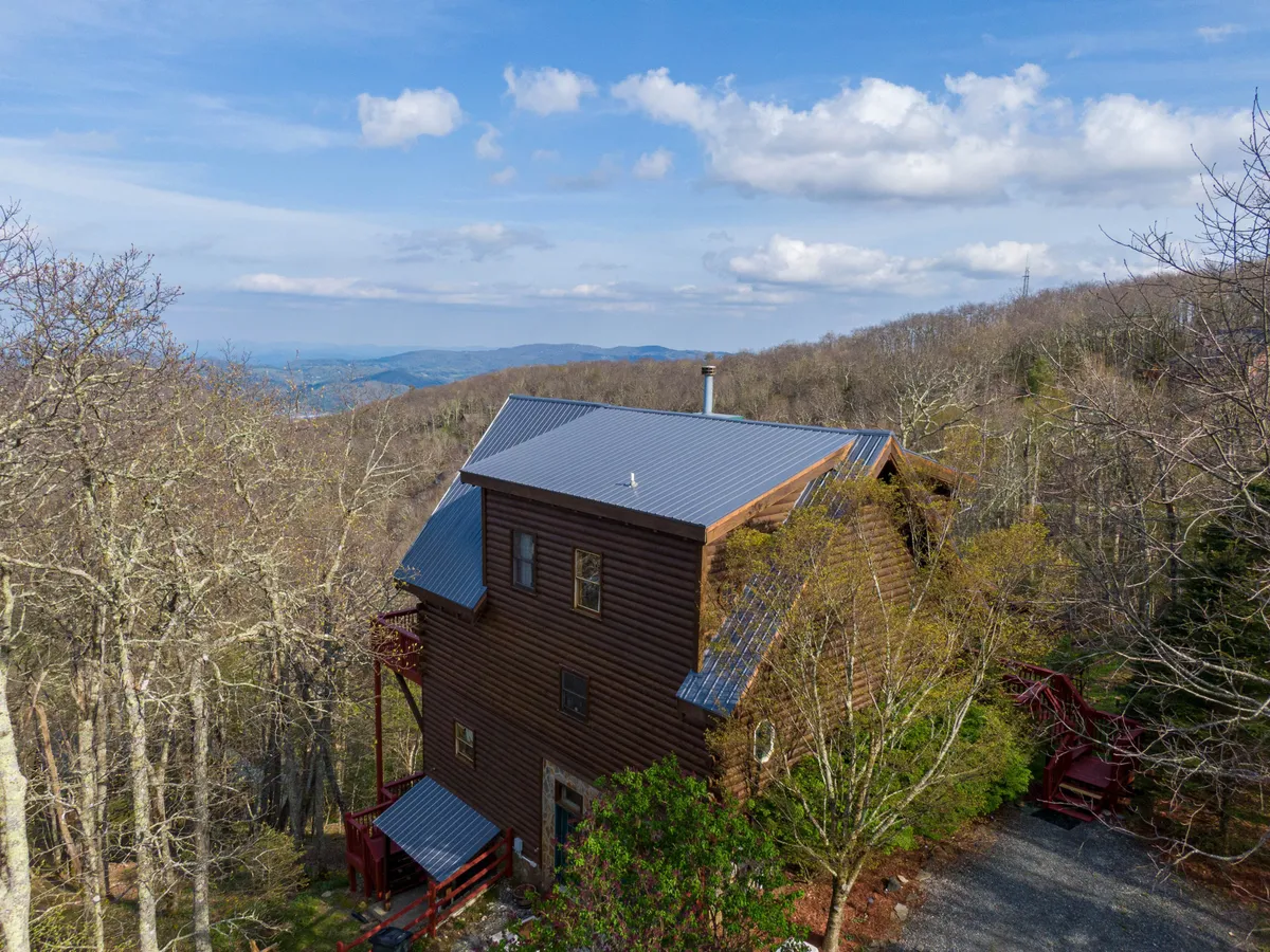 This exterior photo shows a wooden house nestled among trees with a spacious deck and sweeping mountain views in the background. The scene exudes tranquility and a strong connection to nature, highlighting the cabin's proximity to outdoor adventure.