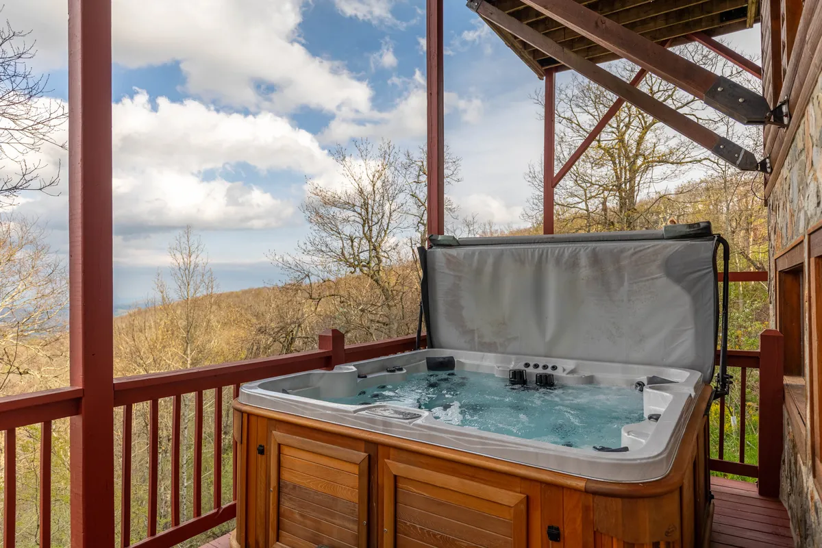 This exterior image features a saltwater hot tub positioned on a wooden deck, offering wide, scenic views of layered mountain ridges in the background. The tranquil setting is perfect for relaxation, with space to soak and take in the sunrise or stars.