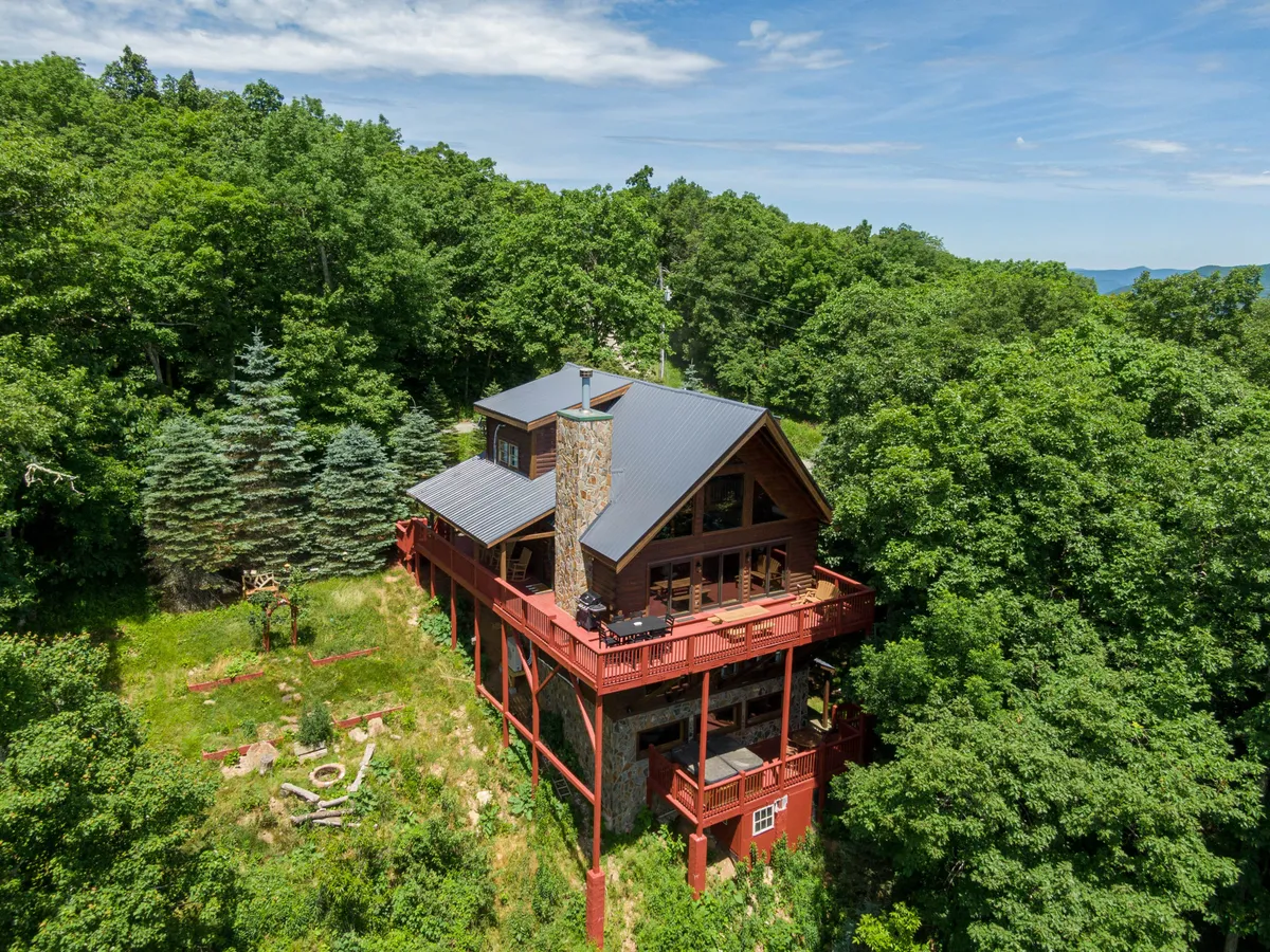 A spacious wooden deck with a stone chimney, surrounded by lush trees and manicured gardens. The deck is ideal for outdoor gatherings, morning coffee, or evening stargazing, offering tranquil immersion in nature and a sense of seclusion.