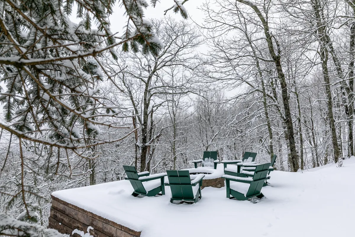 A serene winter landscape featuring a wooden seating area set amid snow-covered trees, inviting guests to gather around a fire pit, sip cocoa, or share stories. The peaceful, reflective mood is perfect for quiet evenings or romantic escapes.