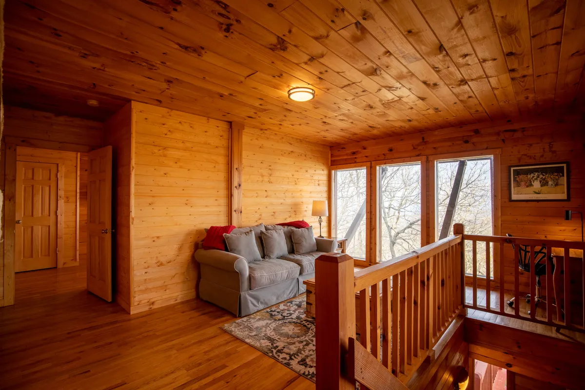 A warm and welcoming sitting area with a soft sofa, windows offering views and natural light, a lamp, and a cozy rug. The space is perfect for morning coffee, reading, or quiet conversation, supporting flexible sleeping arrangements with a nearby sleeper sofa.