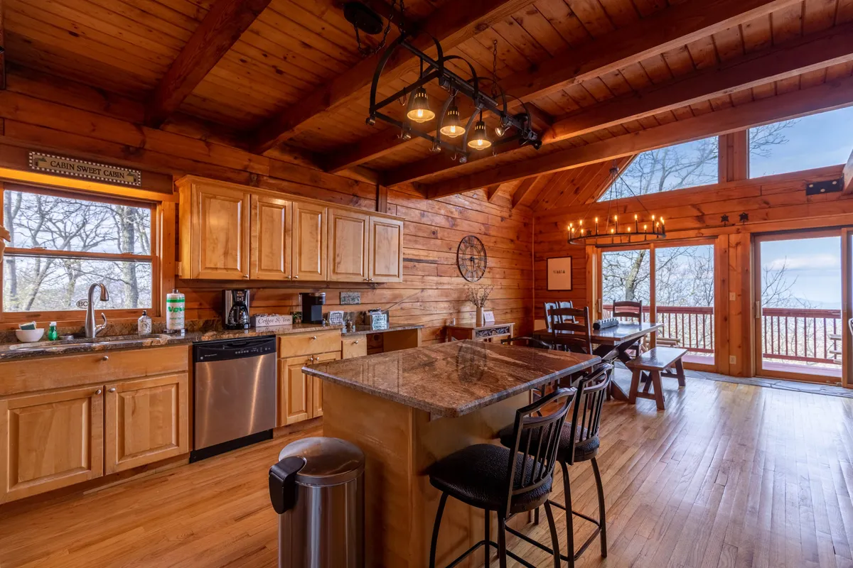 The kitchen and dining area are shown with granite countertops, wooden cabinets, large windows with views, and an adjacent dining space. The area feels cozy and is filled with natural light, ideal for preparing meals or sharing breakfast with loved ones.