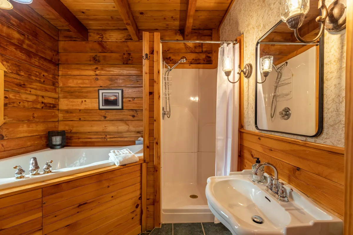 A tranquil bathroom with a luxurious bathtub and shower area, surrounded by warm wooden walls and gentle lighting. Decorative accents and framed art create a spa-like retreat for relaxation after a day in the mountains.