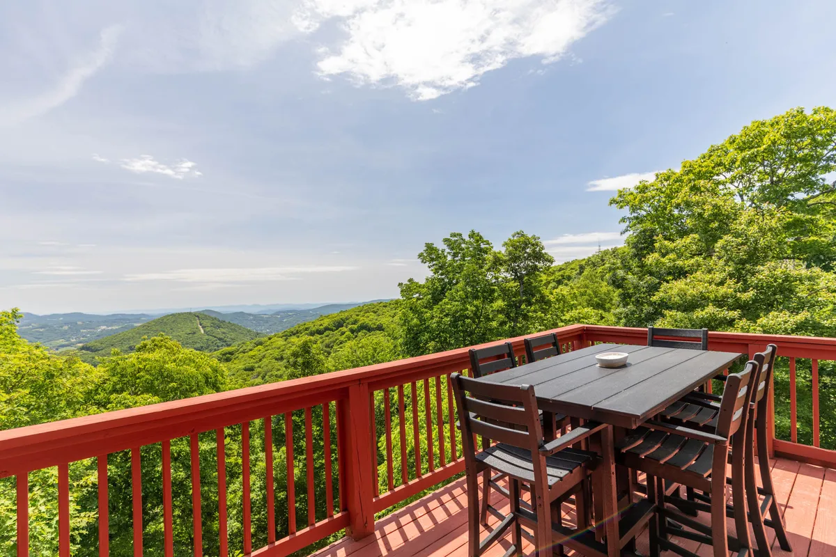 An exterior deck features a dining table set against panoramic mountain vistas and lush greenery. The setup invites guests to dine al fresco while soaking in the breathtaking natural surroundings.