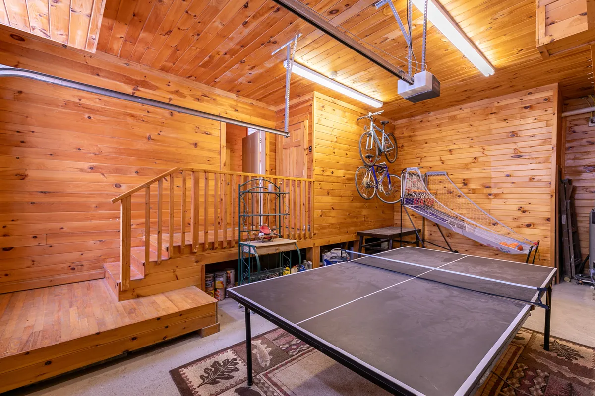 The recreation level of the home features a ping pong table set beside a rustic wooden staircase, with bicycles mounted on the wall and a sports net in view—creating an energetic and playful space for friendly competitions.