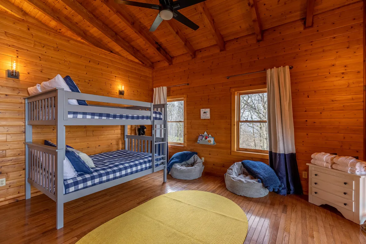 A playful yet restful bunk loft featuring a full-over-full bunk bed, cozy bean bag chairs, and large windows with a view. The cheerful yellow rug and abundance of natural light make this space ideal for children or teens to relax, play, and sleep.
