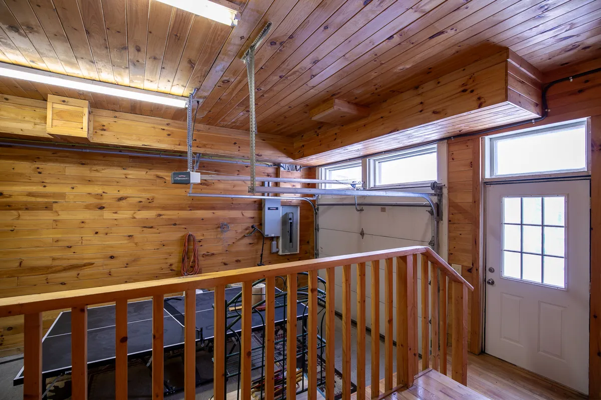 An inviting lower-level game zone with a ping pong table, wooden railing, and garage doors, creating a casual space for friendly competition and group bonding.