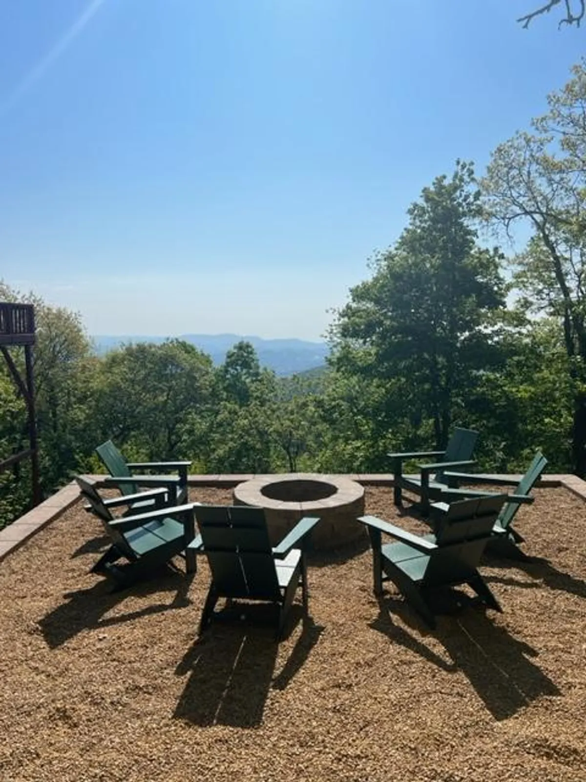 A cozy outdoor fire pit area surrounded by Adirondack chairs and overlooking a sweeping mountain view, set for evening gatherings, storytelling, and stargazing.